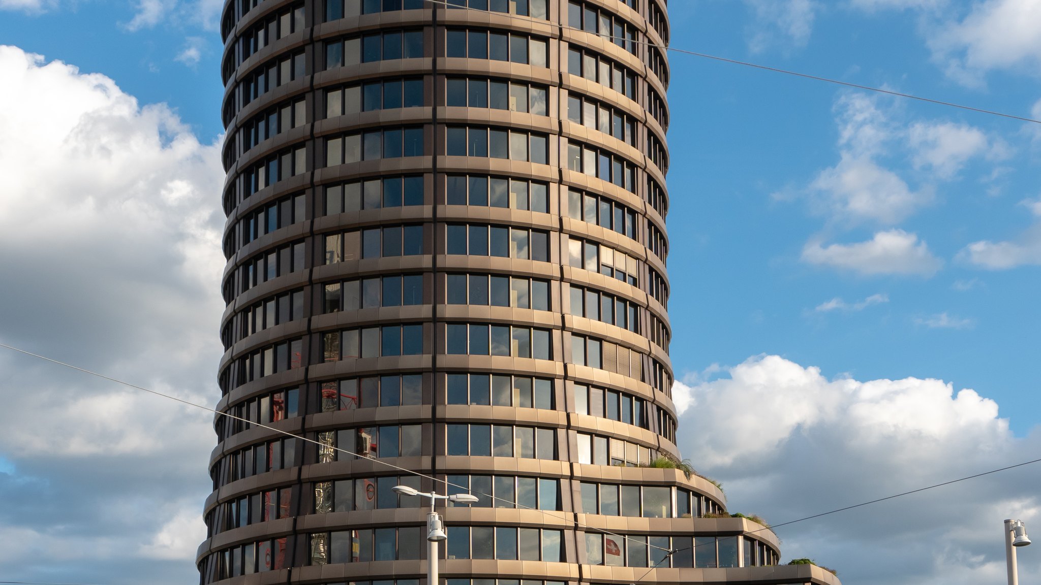The round tower of the Bank for International Settlements in Basel, Switzerland, against a blue sky with clouds.