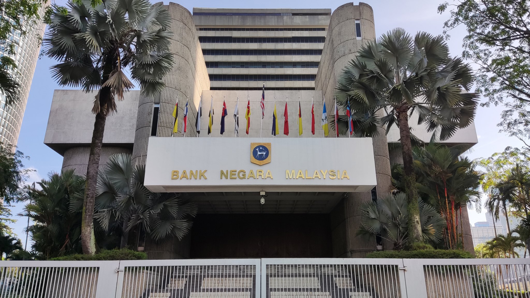 The entrance of Bank Negara Malaysia's headquarters in Kuala Lumpur, with palm trees and the bank's name above the doors.